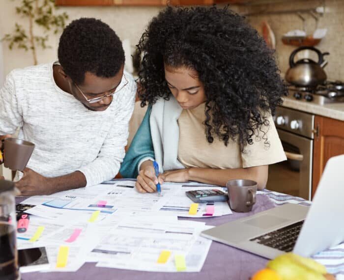 Young African family having debt problems, not able to pay for gas and electricity, managing finances, sitting at kitchen table with papers, calculating bills, trying to cut their domestic expenses